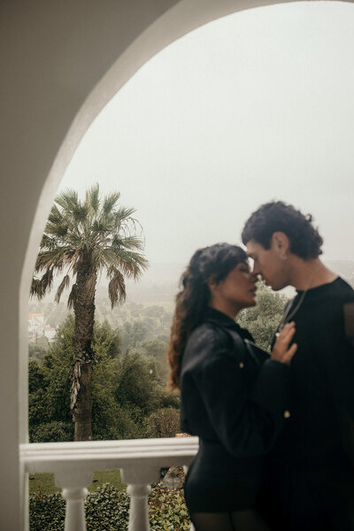 A couple stands close face to face in front of a forest-landscape.