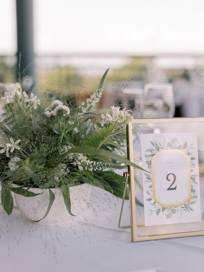 Wedding reception table with a lush greenery arrangement and gold-framed table number sign