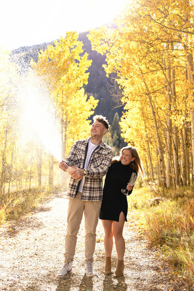 A sweet couple pops champagne after their proposal near pinecreek cookhouse in aspen, colorado