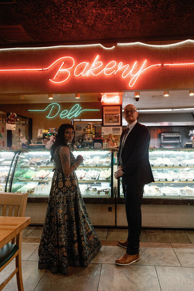 Engagement photography with a couple at a bakery and deli with neon sign behind them