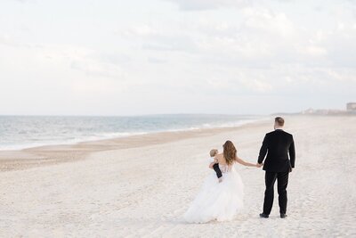 Destination wedding in Florida with a bride and groom holding hands walking on the beach, holding their son