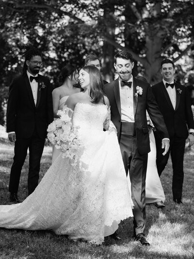 black and white bride and groom walking under trees smiling and laughing with their family and friends