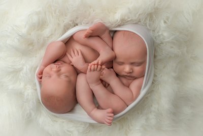 twin newborns sleeping while swaddled together in a white wrap on a white blanket