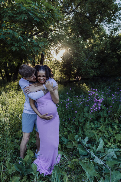 pregnant couple laughing for photograph outdoors