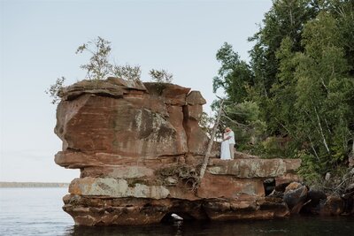 bride and groom embracing on a rock formation above a lake