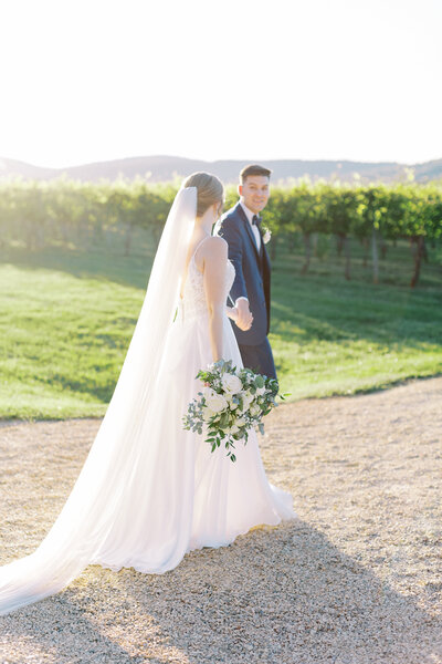 Groom wearing patterned tie and bride with lace open back dress smiling at camera for portrait. Image captured at Keswick Vineyards by Ashley Eagleson Photography.
