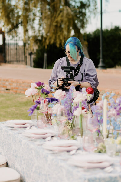 woman in a purple sweater holding a camera filming a tablescape of flowers