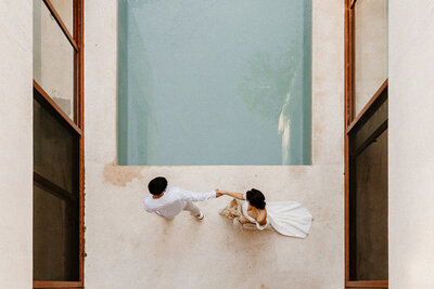 Overhead shot of a bride and groom holding hands by a modern minimalist pool at a Tulum Airbnb wedding venue.