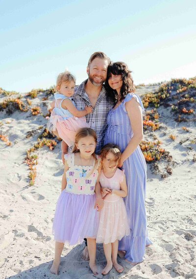 A family smiles together for a photo on the beach, captured by a family photographer.
