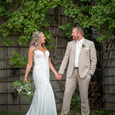 bride and groom hold hands in front of wall with vines