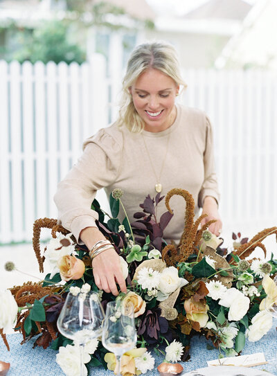 Female model smilling while arranging a flower bouquet on top of a table.