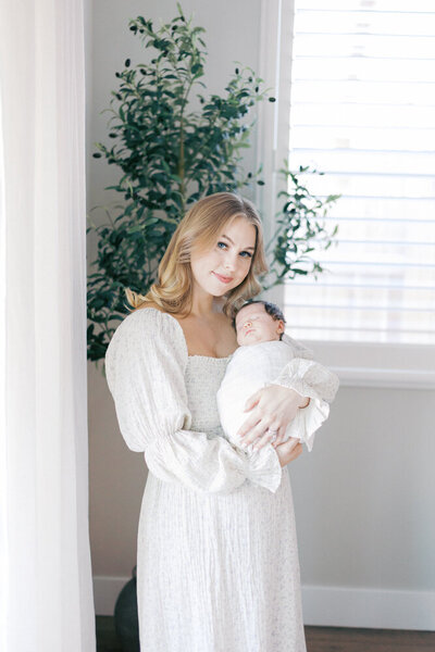 expecting mom standing under tree holding her belly wearing a pale gray dress