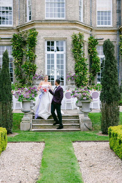 A wedding photo of a couple walking down stone steps in front of Hedsor House in the UK