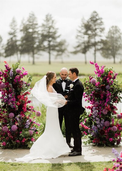 Wedding ceremony with purple floral pillars on lawn at Sunriver Great Hall