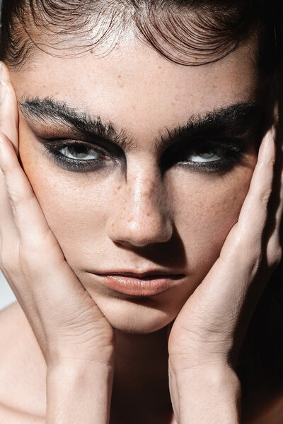 Beauty portrait of freckled model with bold eyebrows resting face on hands