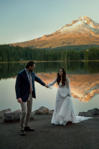 Elopement Couple holding handing with Mt Hood in the background with the mountain reflection in the lake behind them