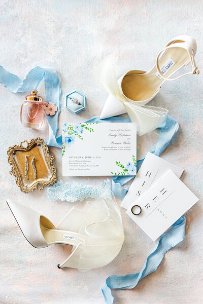 a flat lay of ribbon, wedding invitations, shoes, and jewelry
