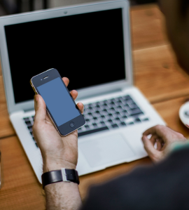 Person holding a smartphone in front of a laptop, symbolizing digital communication and messaging alignment.