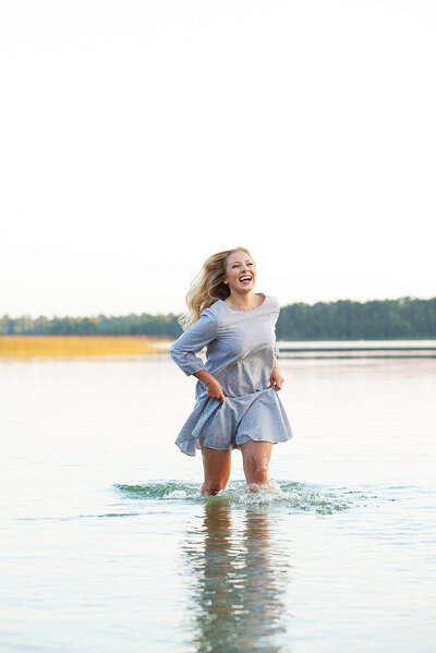 Blonde haired High School senior girl running in a Minnesota lake laughing.
