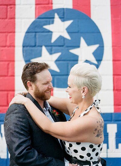 bride wearing a white dress with black polkadots and the groom in a black suit pose in front of the iconic tristar Nashville mural