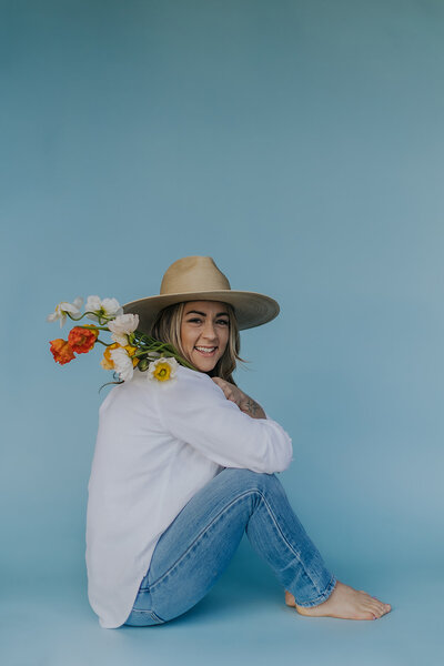 Alexandra wearing jeans and a white top, smiling at the camera from a side profile and holding flowers