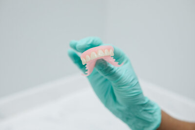 A prosthodontist at Peak Prosthodontics in Lethbridge holding dentures emphasizes proper denture care, including daily brushing with a denture-specific cleanser, ultrasonic cleaning, and thorough rinsing to maintain fit, function, and oral health.