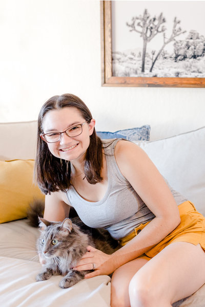 Amber Rivas of Amber Rivas Photography sits on the couch with Rue the cat.