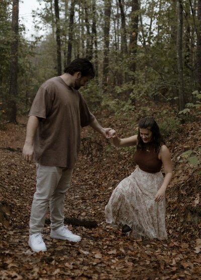 bride in lace gown and groom in dark suit laughing in an embrace beneath rocks during an adventurous elopement