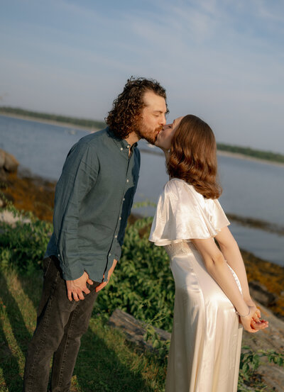 Engaged couple standing on a rocky Maine cliff overlooking the Atlantic Ocean