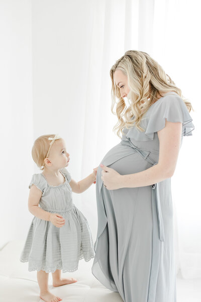 Toddler girl places her hand on her mother's pregnant belly during maternity portrait session