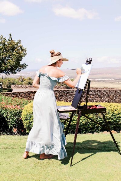 a live painter paints outside on a grassy lawn during the wedding ceremony