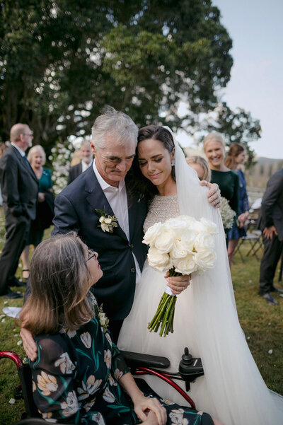 A candid emotional moment with a bride and her father comforting her and her mother who is in a wheelchair