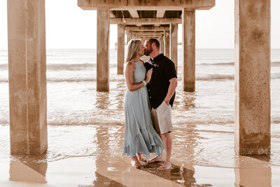 COUPLE KISSING AND EMBRACING UNDER THE HORACE CALDWELL PIER IN PORT ARANSAS TEXAS BEACH