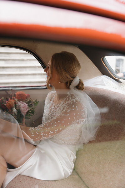 Bruid zit in oldtimer auto met haar boeket .