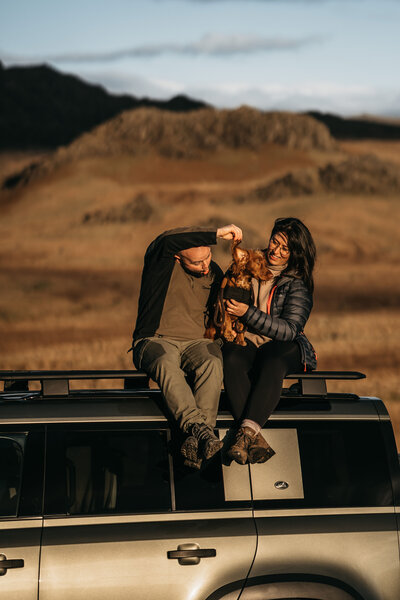 Photographer and videographer duo with their dog on a 4x4 in the Lake District, capturing weddings in the UK and beyond.