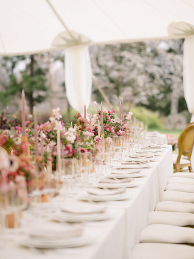 A table at a tented wedding covered in neutral place settings and pink and magenta florals during spring.