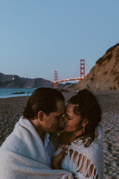 Bride and groom kissing on San Francisco beach with Golden Gate bridge behind them