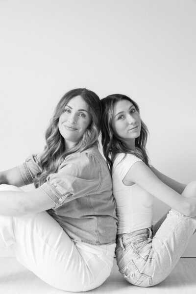 two women sitting on the floor while smiling with their back to each other