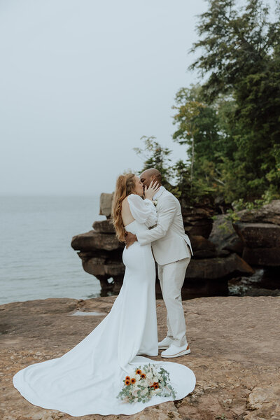 bride and groom kissing after saying vows on a rocky overlook on lake superior