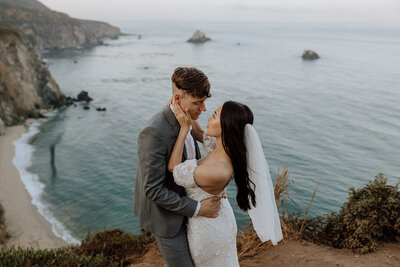 bride and groom embracing on a rocky cliff overlooking the ocean