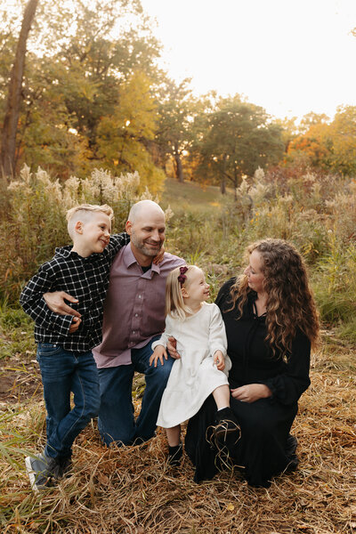 Family of four squatting next to eachother in field and smiing at eachother
