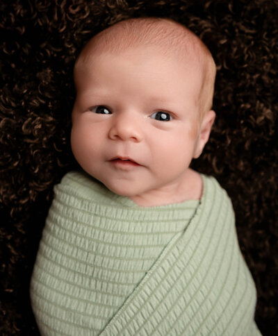 newborn baby in light green swaddle