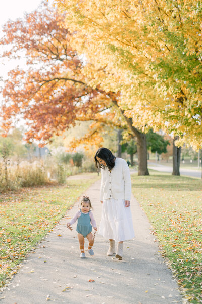 Mom and daughter walking on a sidewalk in autumn, surrounded by yellow and orange leaves