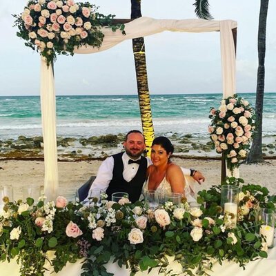 Bride and groom witting down on their reception table with floral details