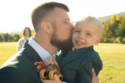 The groom is kissing his son on the cheek after his wedding ceremony.