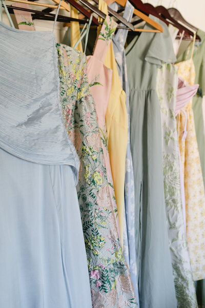 Assorted pastel bridesmaid dresses hanging in a row.