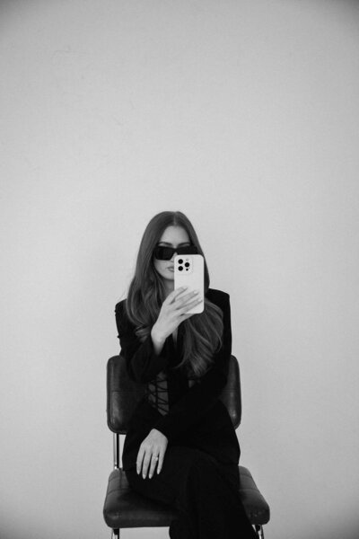 Natalie Jones sitting in a chair with sunglasses on and holding her phone in her face