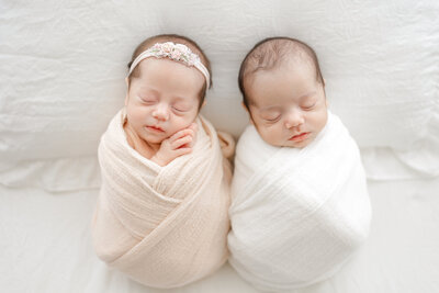 Tampa newborn twins wrapped in soft blush and white swaddles during luxury in-studio portrait session