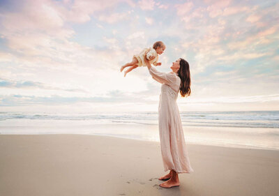 A mom happily plays with her baby during their beach family photography session