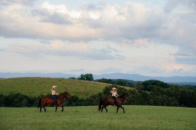 two woman riding horses through an  open field